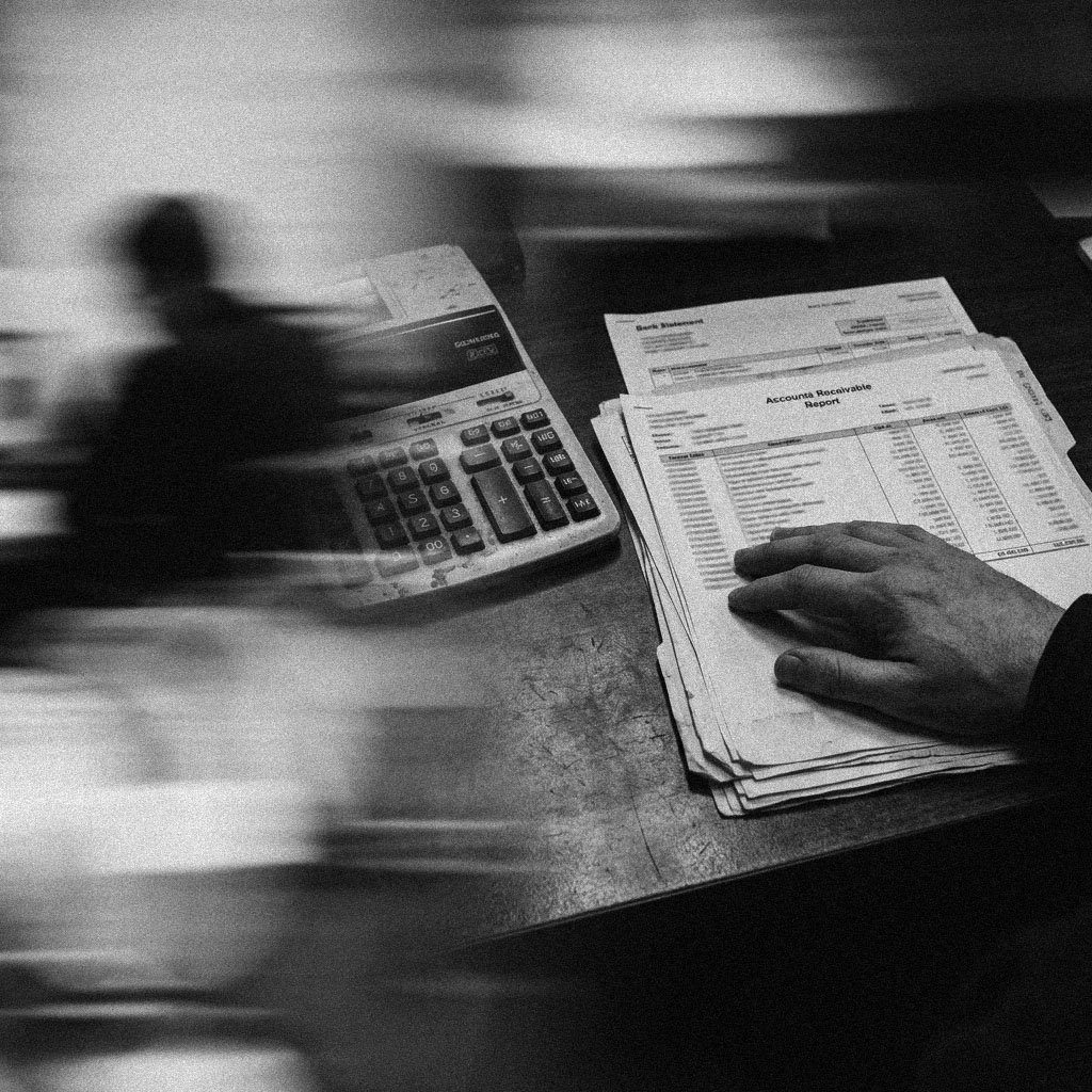 A hand resting on a printed accounts receivable report and bank statement beside a calculator.